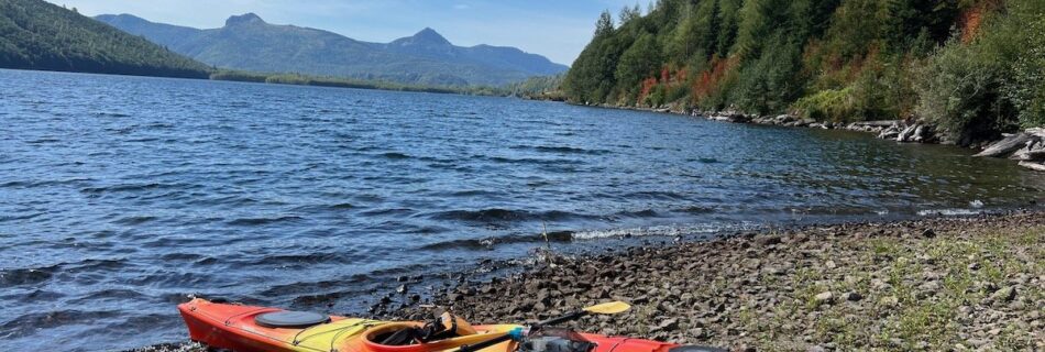 Kayaker paddling on calm Black Hills water with rustic cabin in view